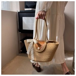 Detail of straw woven tote bag featuring a leather flap with lace bow and pearl buckle