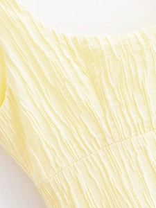 Detail shot of pale yellow fabric featuring vertical irregular pleated texture on dress
