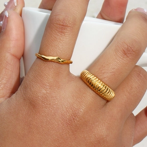 Detail view of stacked gold bamboo-style and textured rings on hand with neutral background