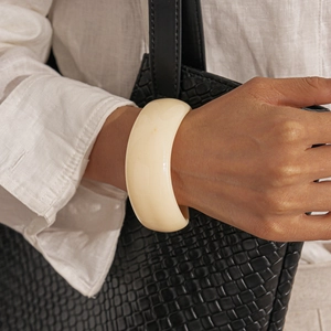 Detail of chunky cream acrylic bangle on wrist with stylish linen shirt and leather bag
