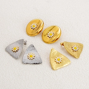 Close-up of gold and silver oval and triangle earrings featuring white daisy patterns