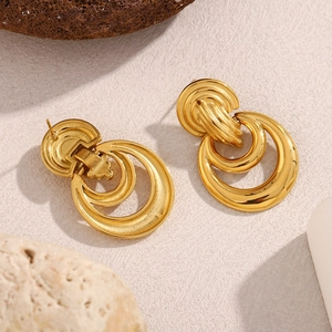 Détail macro de boucles d'oreilles double boucle dorées 18K sur fond en pierre texturé