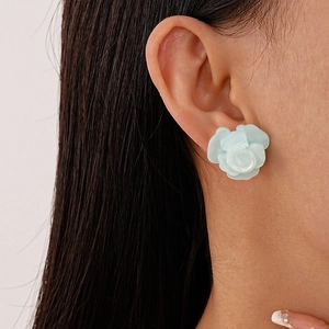 Macro detail of a light blue resin rose flower stud earring worn on a model ear lobe