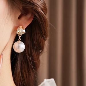 Close-up of model wearing gold geometric crystal stud earrings with large white pearls