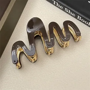 Macro view of S-shaped wave hair claw clip in dark brown acetate and gold metal finish