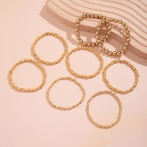 Set of eight gold beaded bracelets with heart charms on a pink background