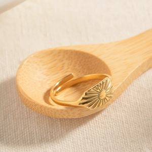 Minimalist 18k gold plated stainless steel square ring with sunburst pattern on a wooden spoon