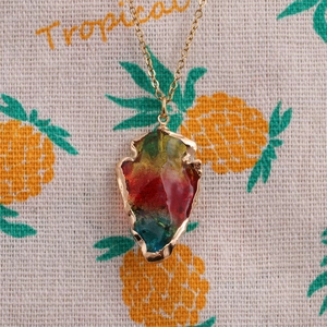 Detailed close-up of a golden triangle pendant with multicolor crystal on a tropical fabric