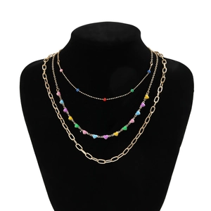 Detailed macro view of a triple-layered gold necklace with colorful beads and heart charms