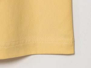 Vue macro du tissu sergé jaune avec double surpiqûre de qualité sur l'ourlet du vêtement