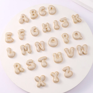 Macro view of gold-plated 3D alphabet charms with cubic zirconia on a white display