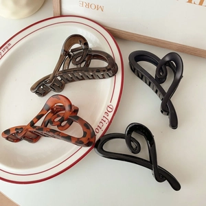Detail of four acetate heart claw clips in tortoiseshell and black on a white ceramic plate