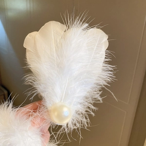 Detailed close-up of a white feather hair clip featuring a large glossy pearl accent