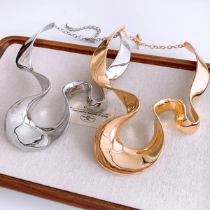 Detailed close-up of chunky wavy metal necklaces in polished gold and silver finishes
