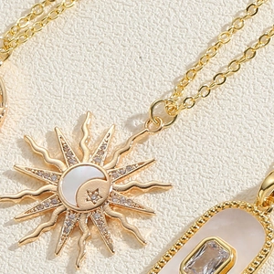 Détail du collier doré montrant le pendentif soleil en nacre et le charme en zircon