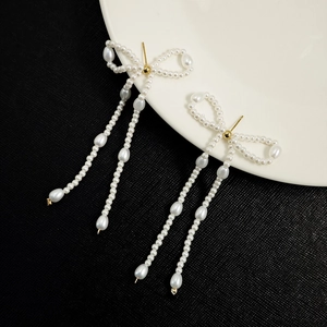Detailed view of pearl bow earrings with long tassels on a white plate background