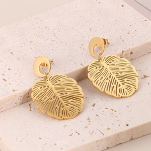 Detail of 18K gold-plated stainless steel monstera leaf drop earrings on stone background