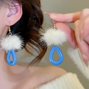 Close-up of white fluffy fur ball and blue teardrop resin pendant earrings on model