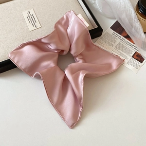 Detailed view of oversized pink satin scrunchie on elegant tray with newspaper decor