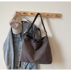 Detail of a large brown canvas tote bag hanging on a hook with a denim jacket