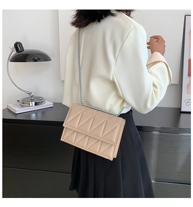 Detail view of quilted beige crossbody bag with silver chain strap on modern background