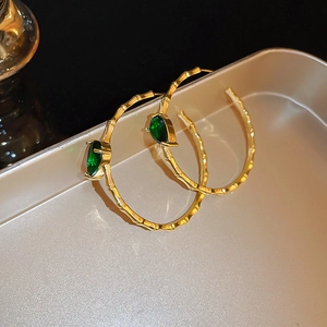 Detailed shot of golden bamboo texture hoop earrings with green emerald-like stones