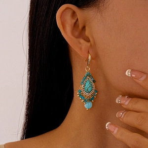Detail of vintage bohemian drop earrings with turquoise stones and golden tassels on model