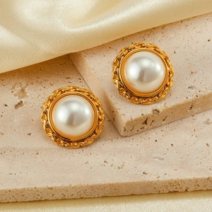 Macro shot of gold pearl stud earrings with woven chain borders on marble and silk