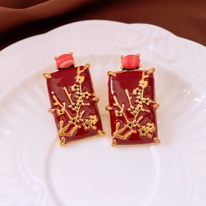 Detail of vintage square earrings with red enamel and gold plum blossom relief on ceramic tray