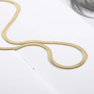 Macro shot of a flat gold snake chain necklace showing smooth polished metal texture
