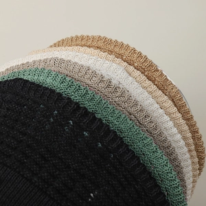 Detail of multi-color hollow knit straw hats showing black, green, and beige weave texture