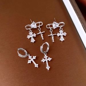 Detailed view of silver zircon cross and heart earrings on a textured brown surface