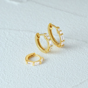 Detailed macro view of gold hoop earrings with inlaid rectangular and round zircons