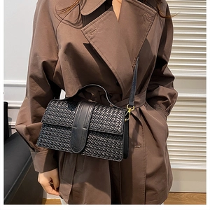 Close-up of black woven texture on a flap bag featuring a gold buckle and shoulder strap