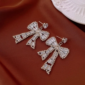 Détail macro de boucles d'oreilles nœud en argent avec zircons sur fond de soie luxueuse
