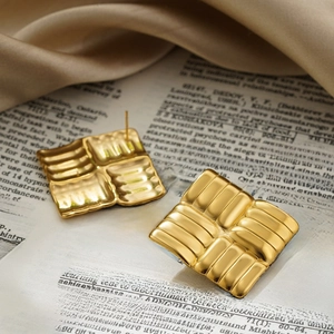 Close-up of golden square braided earrings on vintage book with soft silk fabric