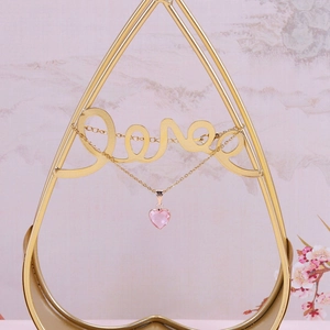 Detail view of pink crystal heart pendant on gold chain hanging on a Love stand