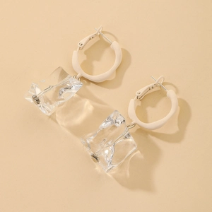 Macro detail of clear acrylic ice cube drop earrings with minimalist cream round studs