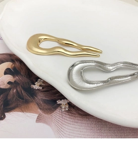 Detail view of gold and silver wavy U-shaped metal hair forks on a white ceramic plate