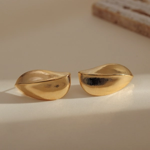 Macro shot of gold leaf-shaped earrings featuring a sophisticated vertical brushed metal texture