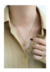 Detail shot of a minimalist gold pendant necklace and matching ring on a linen shirt