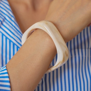 Macro shot of chunky cream resin bangle with marble pattern worn on a model's wrist