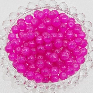 Macro view of translucent magenta glass beads with pre-drilled holes in a clear glass bowl