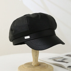 Detail of black faux leather newsboy hat featuring a side rectangular metal buckle