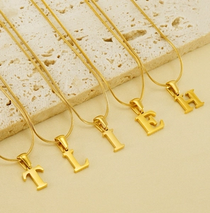 Detail of gold titanium steel alphabet pendants with snake chain on stone base