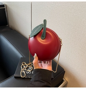 Close-up of a cherry-shaped red crossbody bag with golden chain and green leaf detail