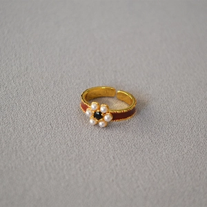 Macro shot of gold-plated brass flower ring with red enamel and white pearl details