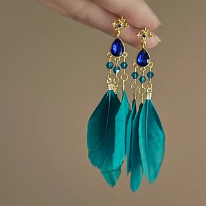 Detail of bohemian long feather earrings with blue teardrop gemstone on gold base