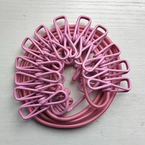 Pink portable travel clothesline with 12 coated metal clips on wooden background