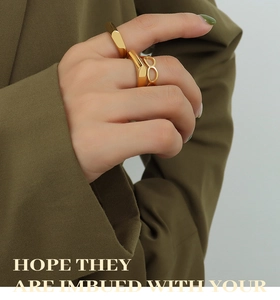 Close-up of stacked gold geometric rings on model fingers with olive green suit texture